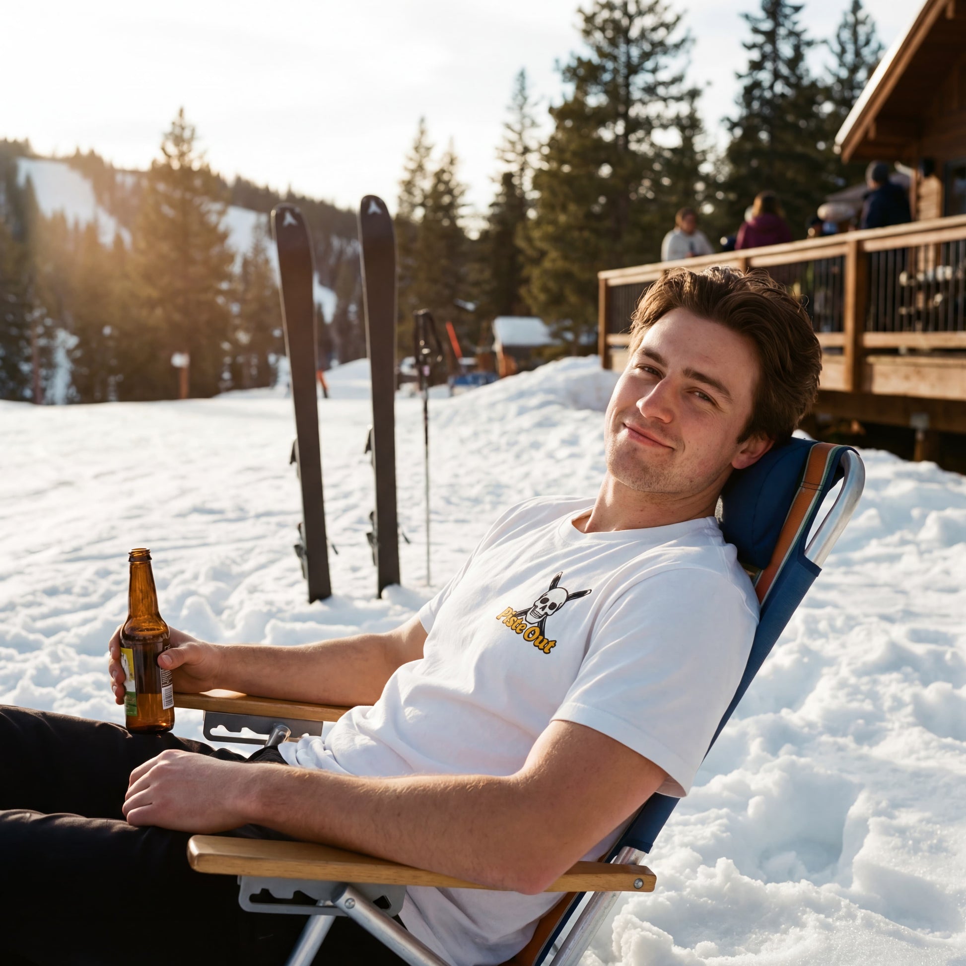 Male model wearing Piste Out Chill to the Bone après ski tee in Snow, sitting in a chair in the snow with a beer