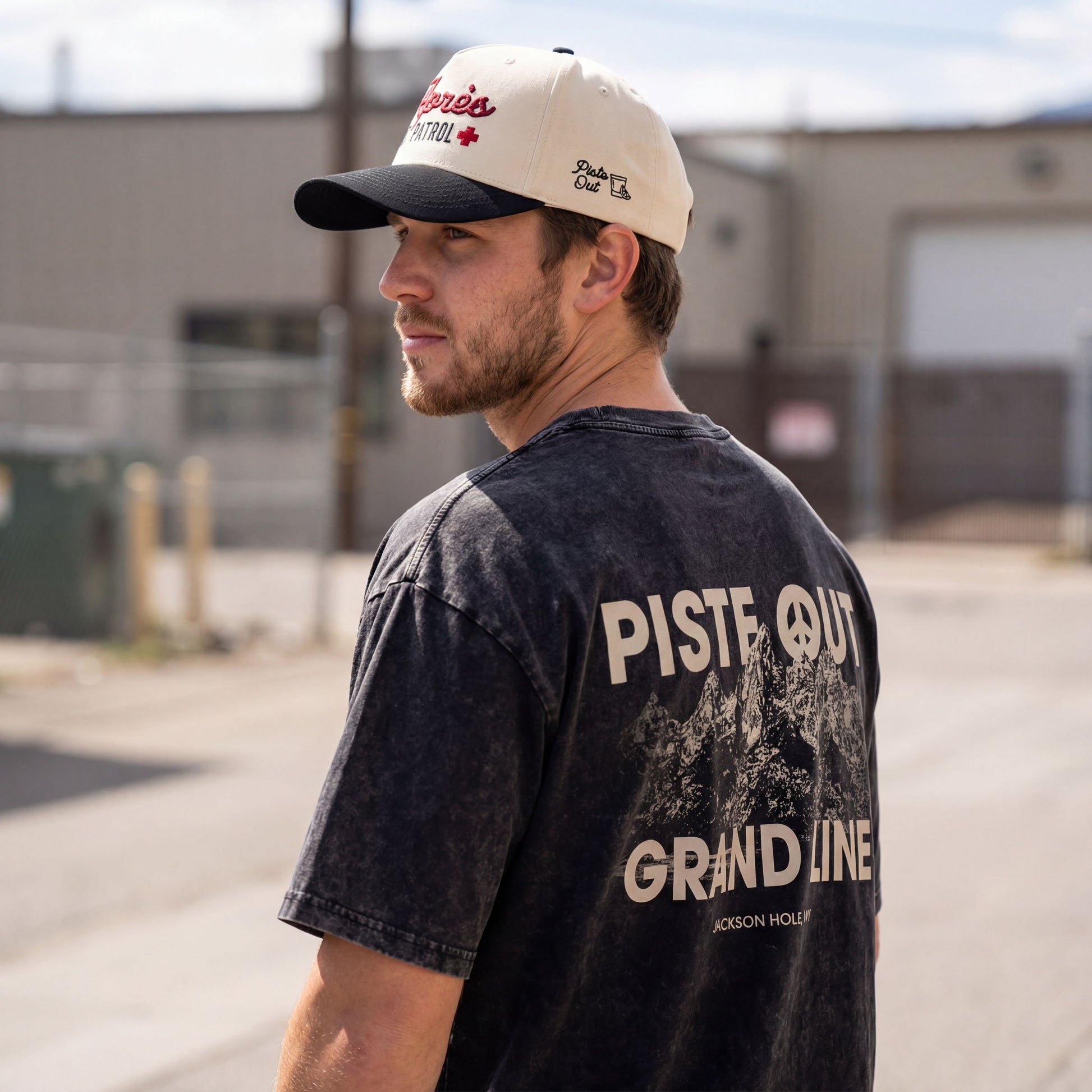 Male model wearing the Grand Line tee in Black Diamond, showing large PISTE OUT and Grand Line Text with a mountain.
