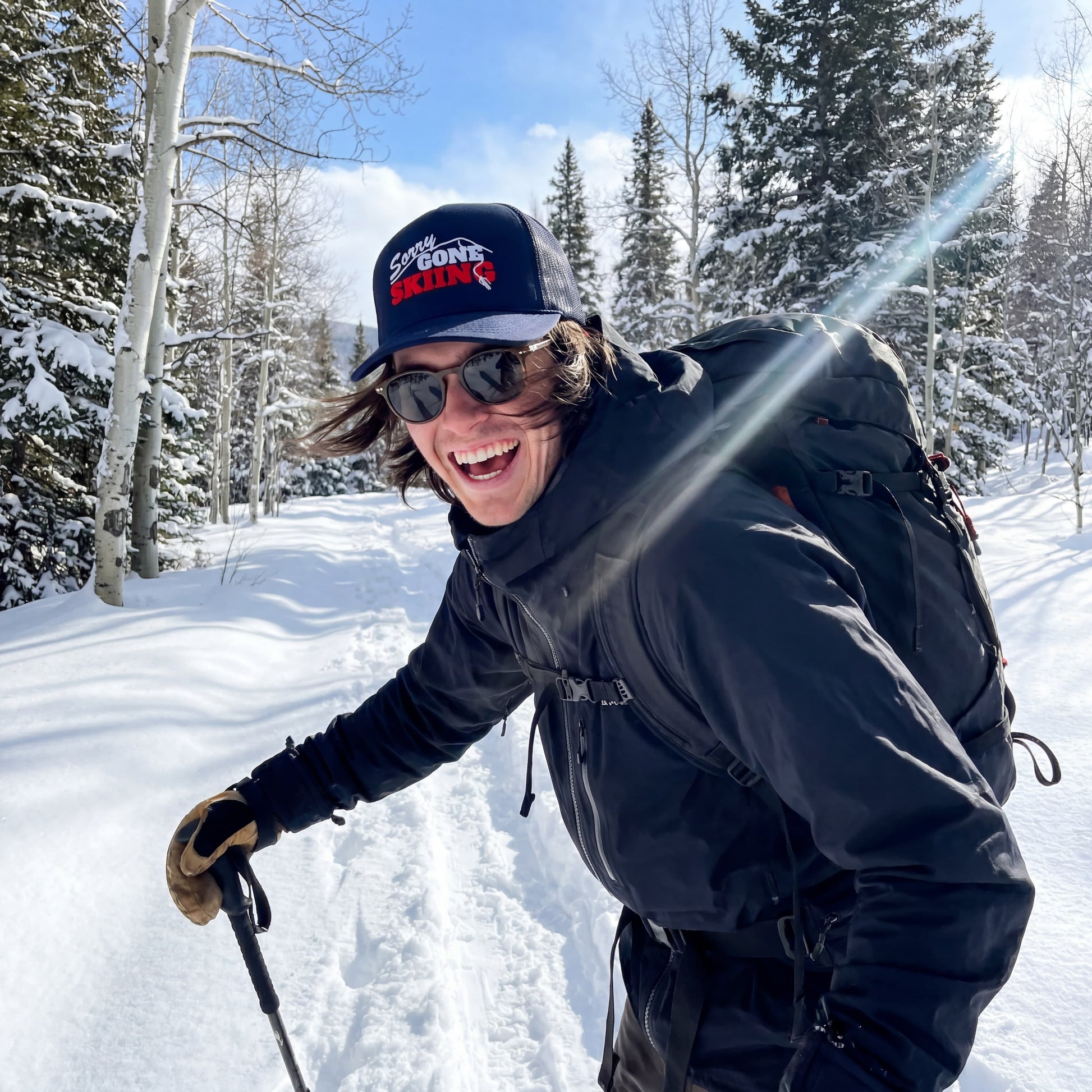 Gone Skiing Trucker Hat in Blue Square worn by a male skier on a snowy backcountry trail with ski poles