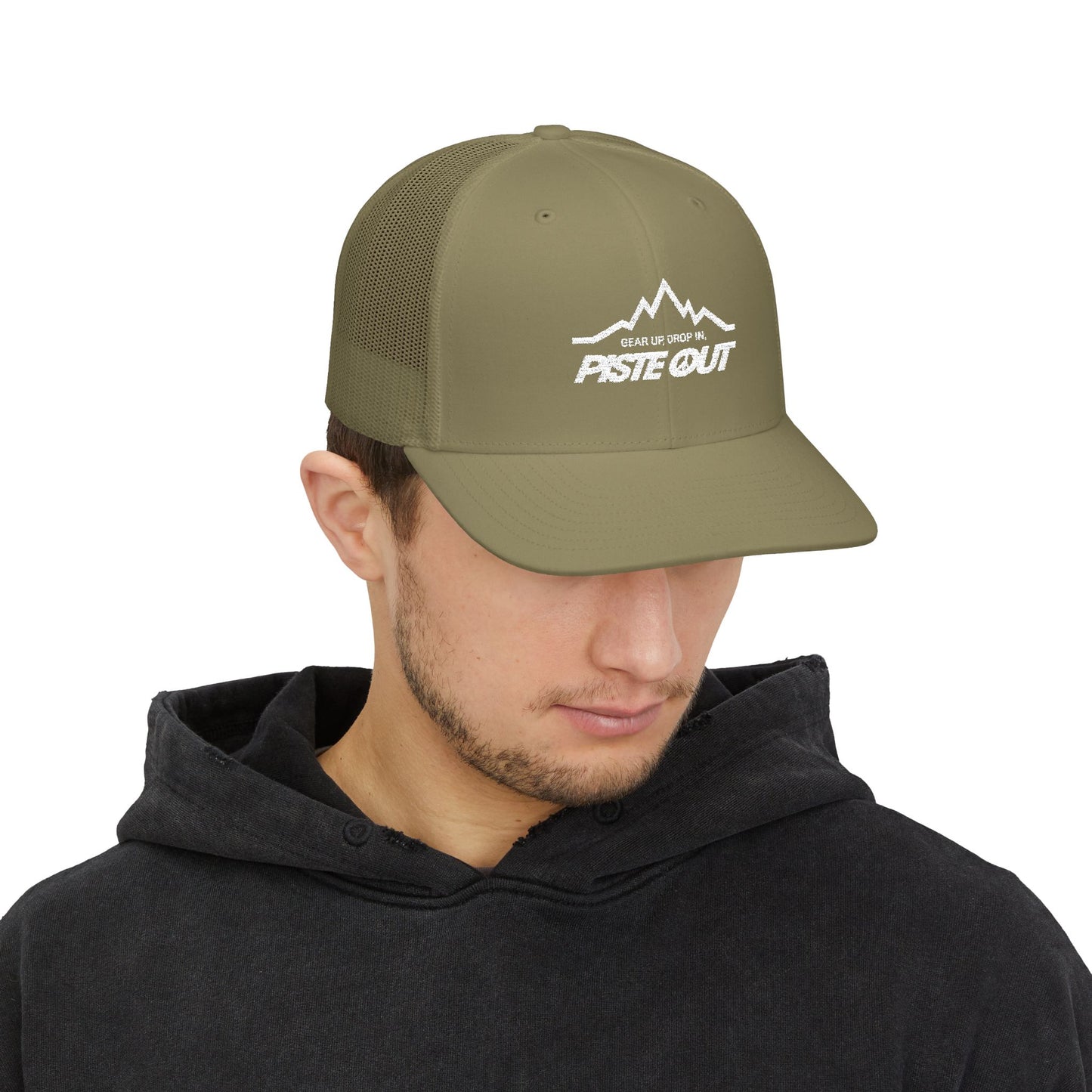 Olive green trucker hat worn by model, with white Piste Out mountain logo and slogan “Gear Up. Drop In.” embroidered on front