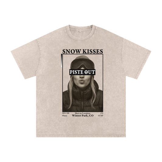 Front view of apricot vintage-washed Snow Kisses tee featuring ski town crush graphic with Piste Out logo across goggles.