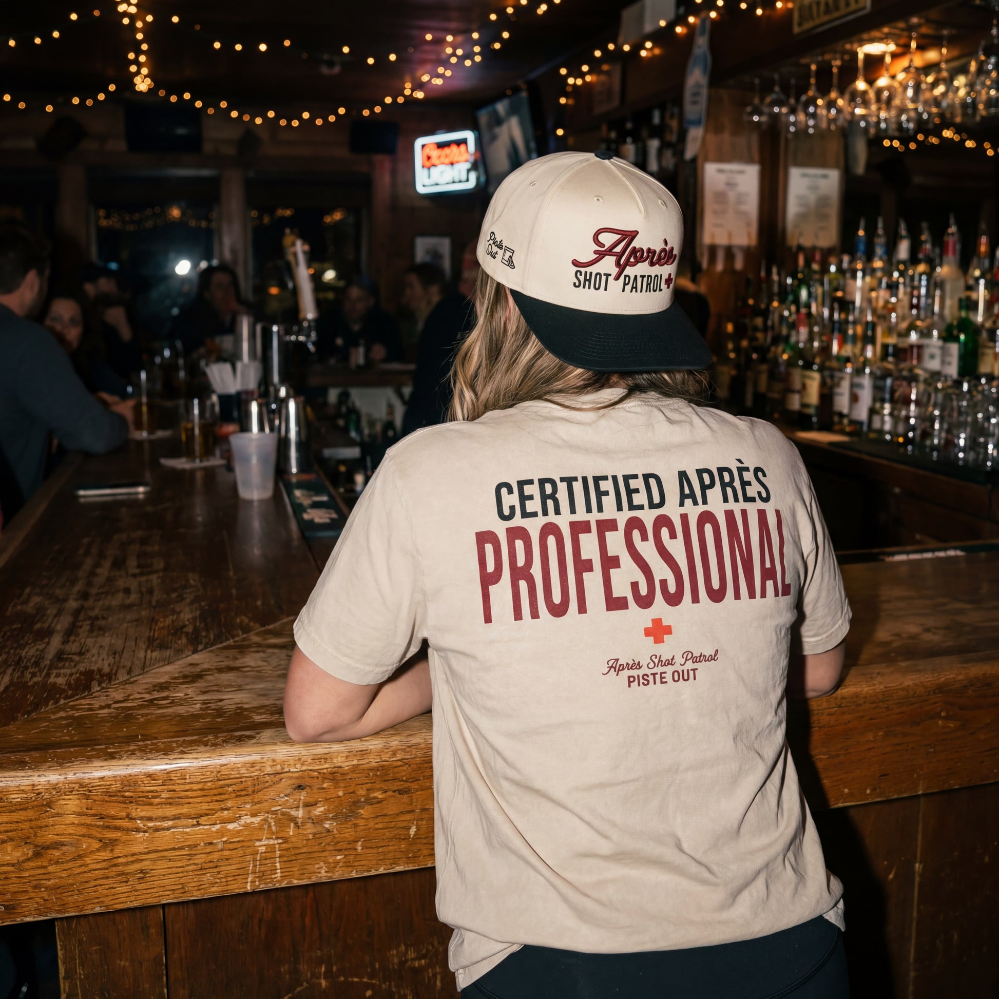 Model wearing a backwards apres shot patrol hat and tee in a bar. 