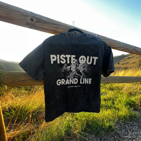 Grandline tee in black diamond hanging on a wooden fence over rolling green hills. 