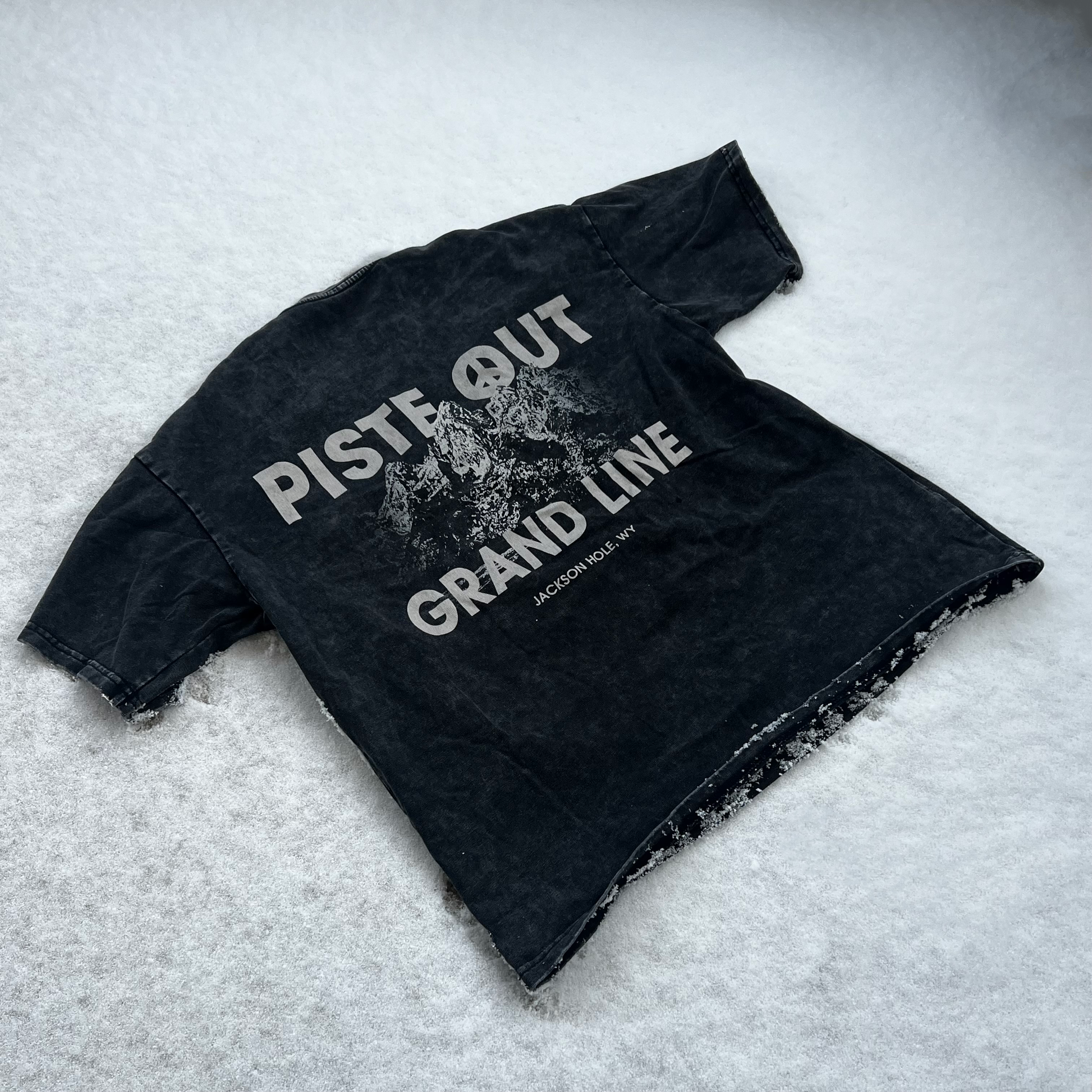 Angle shot of the back of the Grandline tee laying in the snow. 