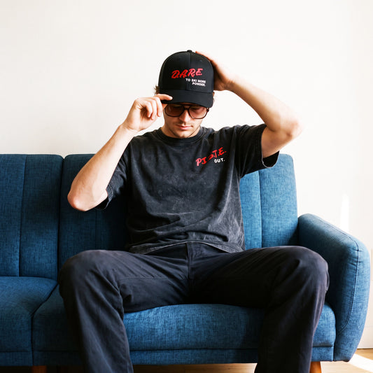 Male Model sitting on a couch wearing the DARE hat and short sleeve tee.