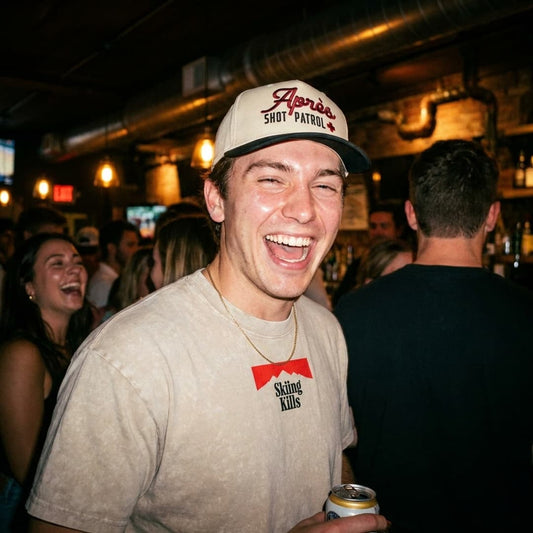 Male model in a bar wearing the Skiing Kills tee in Tan and Apres Shot Patrol Hat.