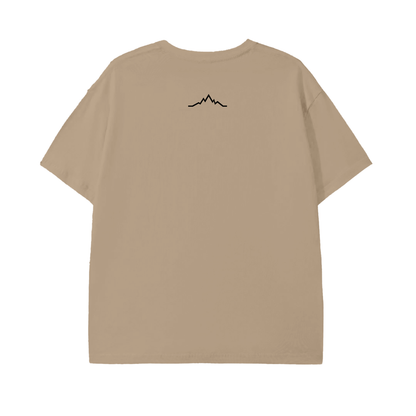 Back view of the Piste Out Logo Tee in Khaki, displaying the small black mountain line design below the neckline on a peach-tone cotton shirt. Minimalist ski culture style.