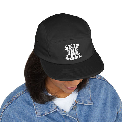 Black Skip the Last 5-panel hat worn by model, front embroidery visible.