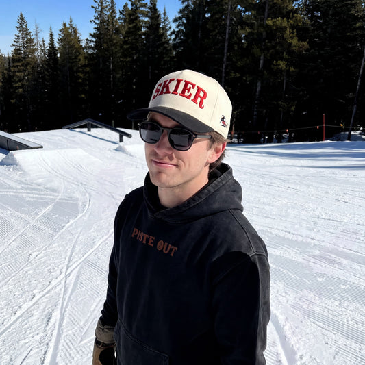 Skier standing on ski slope wearing the Skier Cap in Black Diamond with a black Piste Out hoodie. 