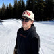 Skier standing on ski slope wearing the Skier Cap in Black Diamond with a black Piste Out hoodie. 
