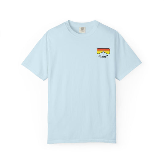 Front of light blue tee featuring retro ski goggle chest logo with red-orange-yellow gradient and “PISTE OUT” text