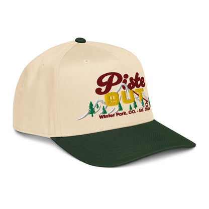 Side-back angle of cream and forest green Sunset Hat showing embroidered Piste Out logo with mountain trees and ski lift details.