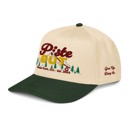 Angled front-side view of cream and forest green Sunset Hat showing embroidered Piste Out logo and side text “Gear Up. Drop In.” in red stitching.