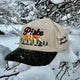 Green Circle Sunset Peaks snapback cap with cream crown and dark green brim photographed outdoors.